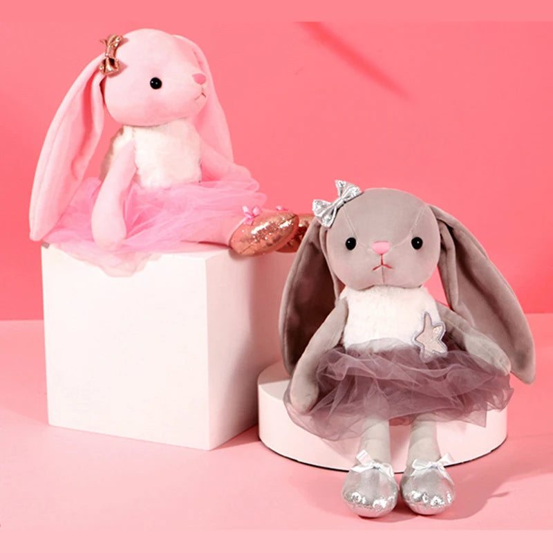 Two plush rabbit toys, one pink and one gray, are displayed on a white pedestal against a pink background.