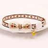 A breakaway cat collar featuring a patterned fabric strap, a bowknot, and a gold bell, displayed on a white plate.