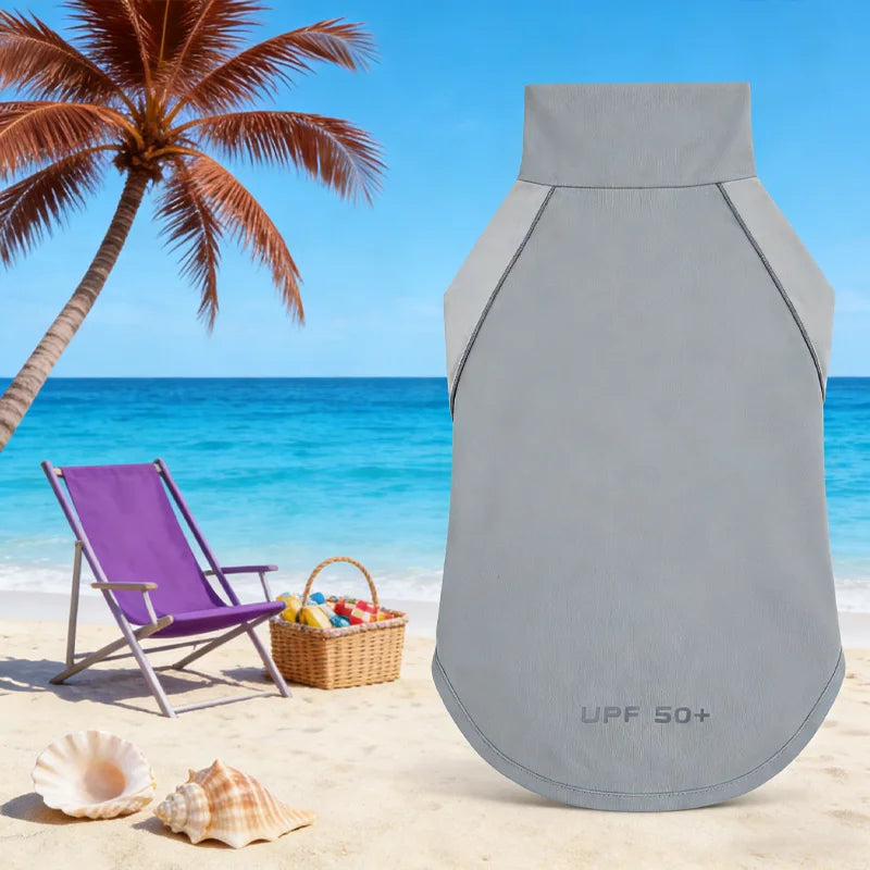 A gray dog cooling vest with UPF 50+ protection is shown on a beach with palm trees and blue ocean.
