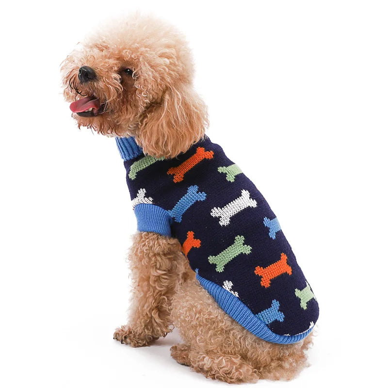 Un caniche marrón claro vistiendo un suéter de punto azul marino con estampados de huellas naranja y verde.
