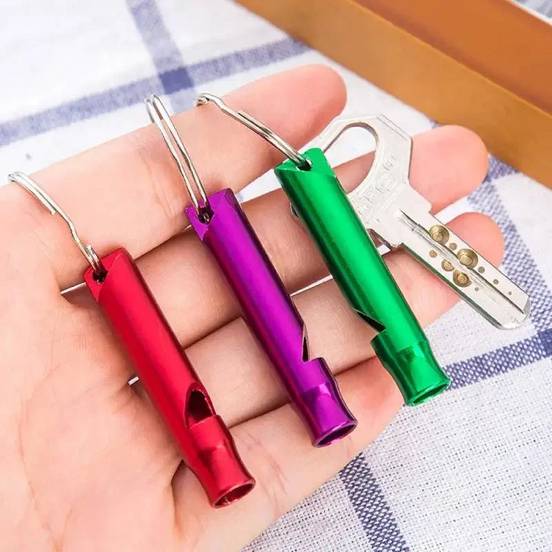 Drei bunte Edelstahl-Hundtrainierpfeifen in rot, lila und grün werden in einer Hand gehalten.