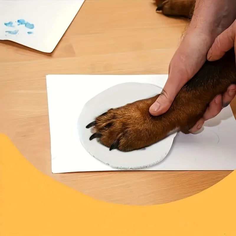 A hand is pressing a paw print into a white disc on paper, demonstrating the creation of a pet memory keepsake.