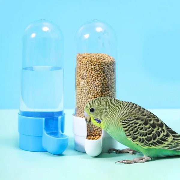 A green bird is perched next to a clear glass water dispenser filled with seeds on a light blue background.