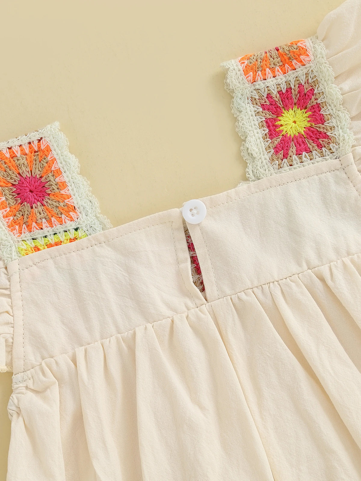A light beige floral embroidery toddler romper with colorful fabric accents.