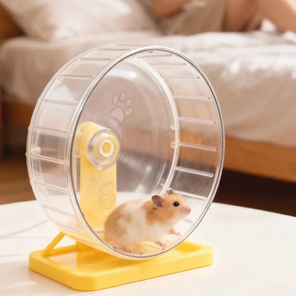 A transparent hamster exercise wheel is shown with a small rodent inside, resting on a yellow base.