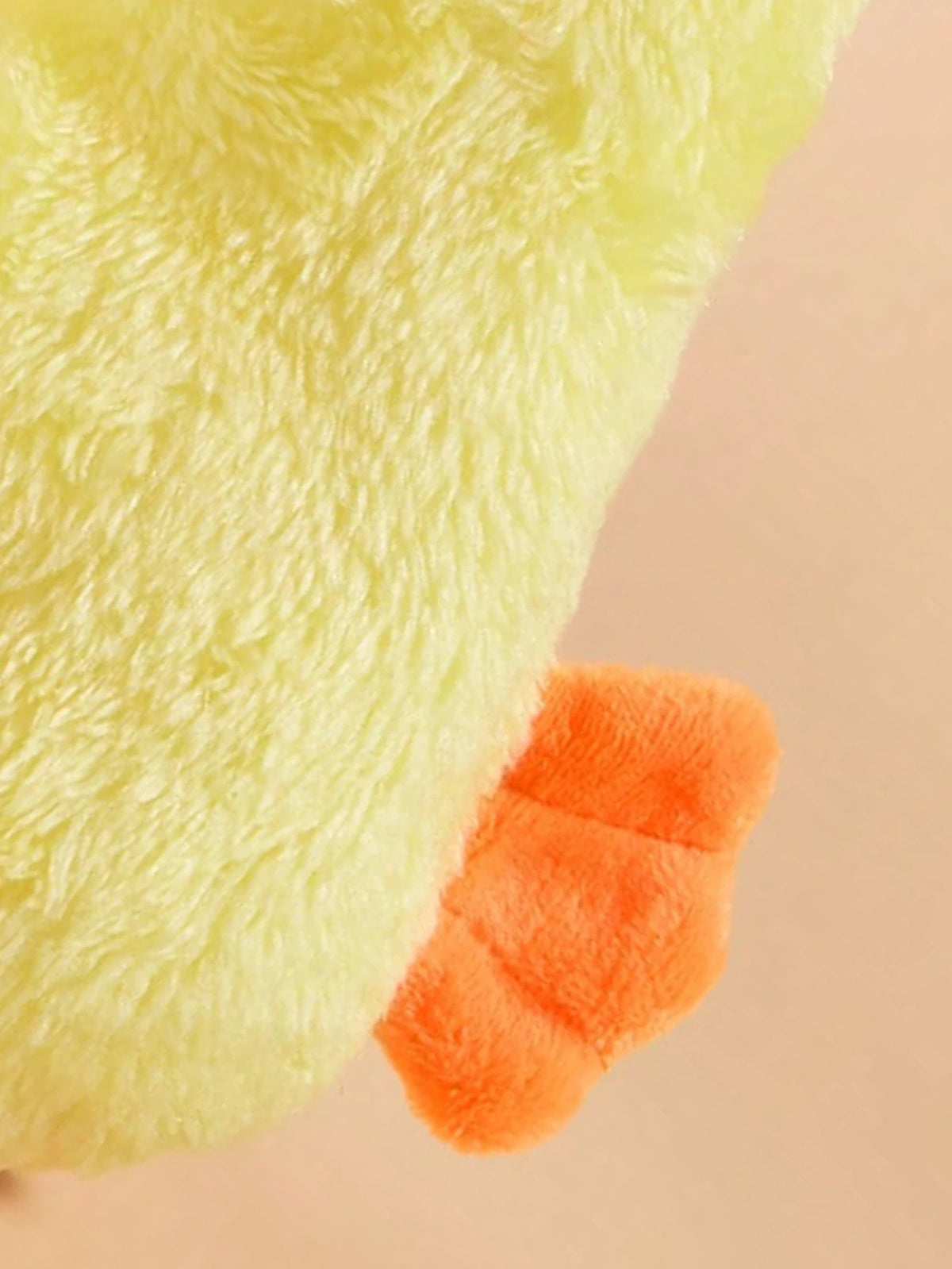 A close-up of a light yellow plush duck toy with an orange foot.