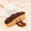 A brown and tan plush toy shaped like a sandwich, resting on a cream-colored knitted fabric next to a white cup.