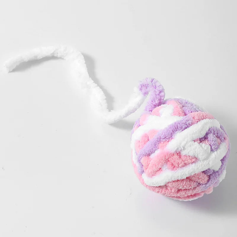 A fluffy ball of pink and purple plush fabric with white accents, resembling a cat toy.