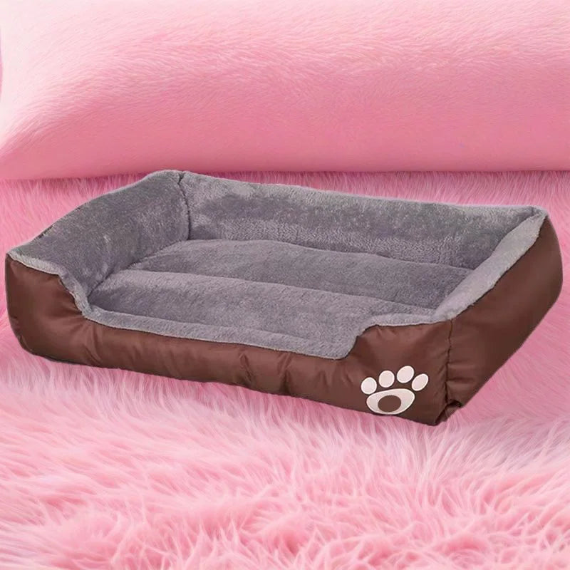 A brown dog bed with a gray cushion and paw print embroidery resting on pink faux fur.