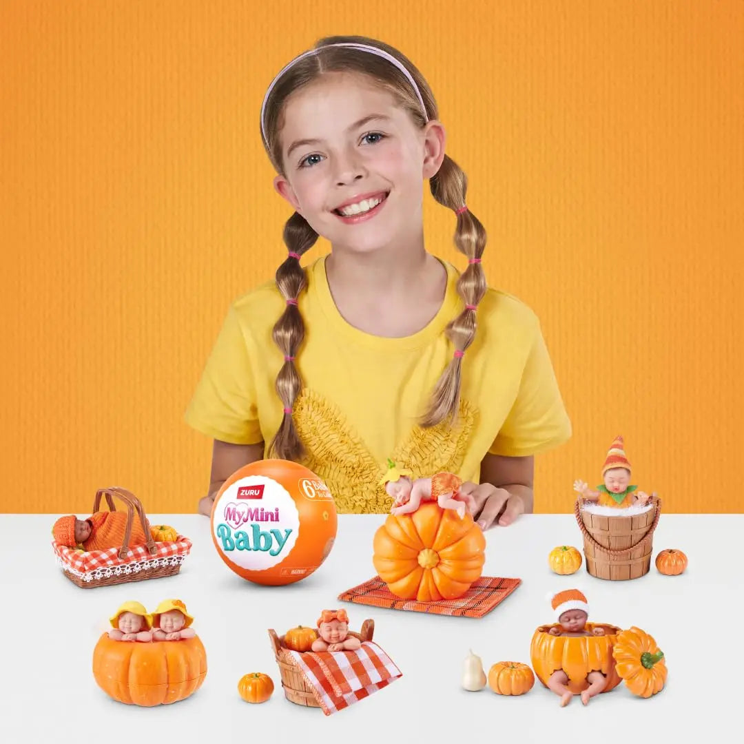 A smiling girl holds a pumpkin patch set featuring miniature baby dolls and pumpkins.