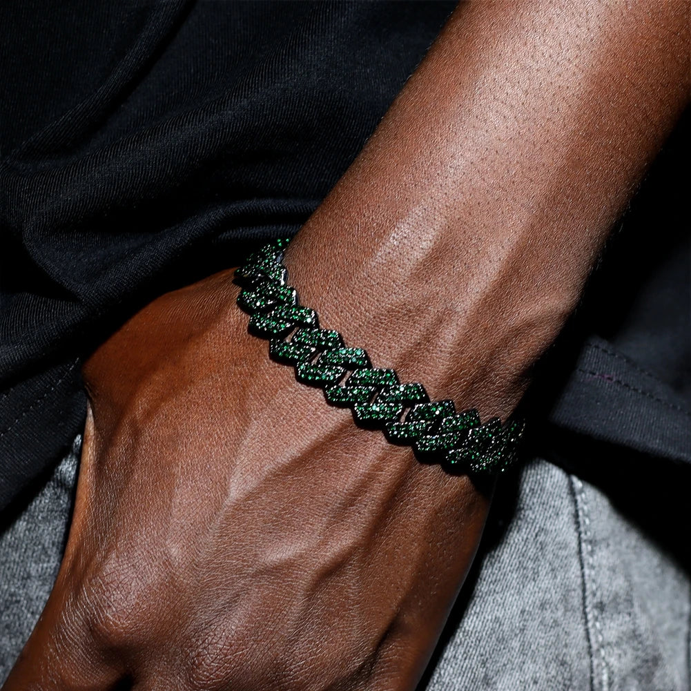 A close-up of a dark green iced-out Cuban link bracelet worn on a person's wrist against a black shirt.