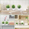 A collection of artificial bonsai potted plants displayed on a wooden table and kitchen counter.