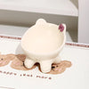 A white ceramic cat food bowl with a raised, tilted design resting on a wooden background.