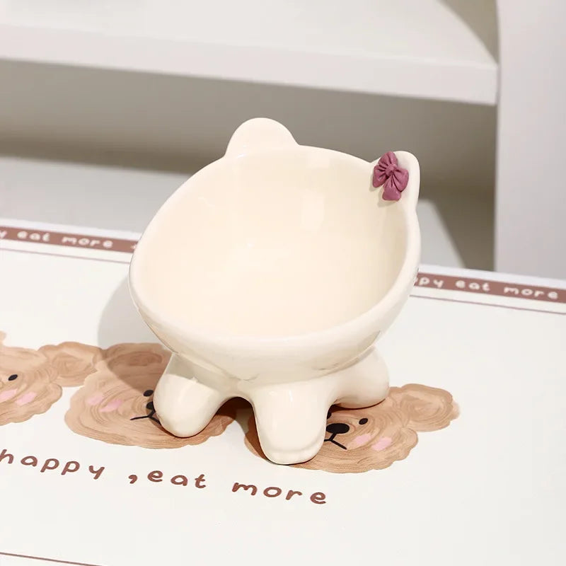 A white ceramic cat food bowl with a raised, tilted design resting on a wooden background.