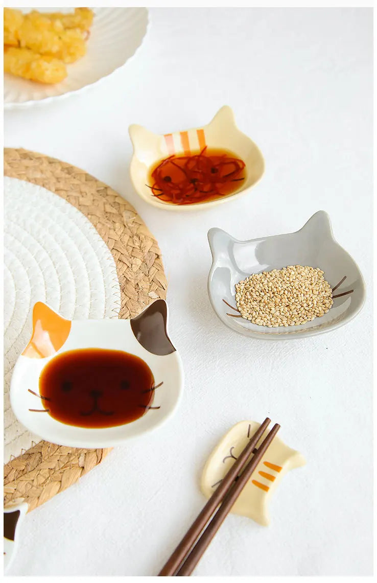 A collection of cat-shaped ceramic sauce dishes and a pair of chopsticks on a white background.