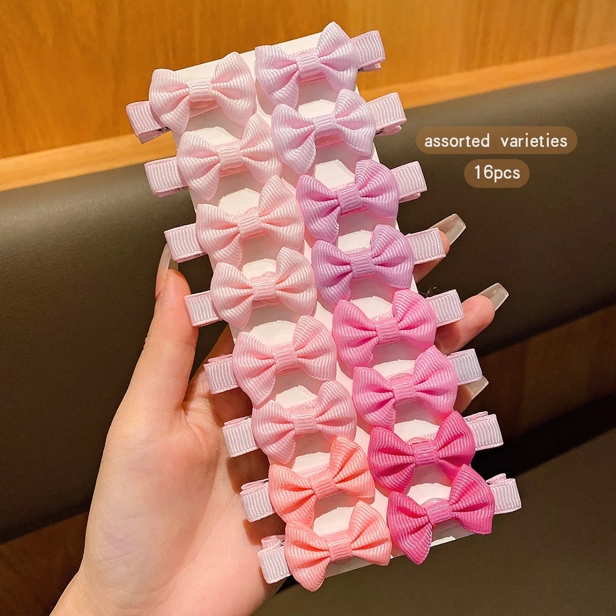 A hand holds a set of assorted pink and coral fabric hair bows for crafting or decoration.