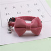 A pink plush velvet pet collar featuring a bow and a silver bell, resting on a white paper with faint text.