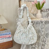 A white floral lace bowknot shoulder bag with a pleated design resting on a textured surface.