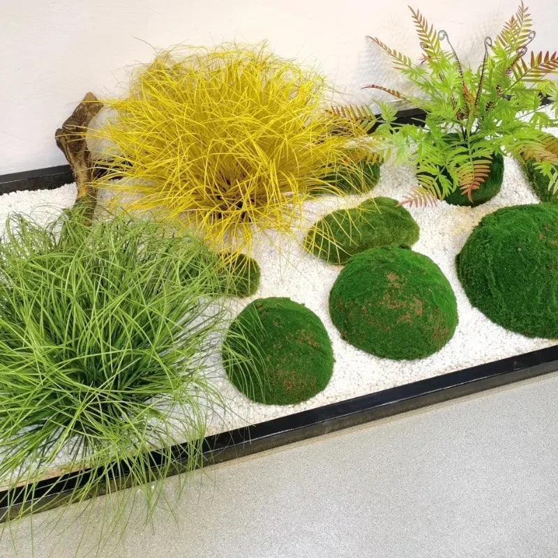 A display of green and yellow ornamental grasses and moss in a rectangular planter with white gravel.