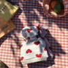 Weißes und rotes Herzmuster-Teddy-Hoodie für kleine Hunde auf kariertem Tischtuch.