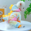 A fluffy white dog wearing a colorful, multi-colored fleece pet overcoat with yellow accents.