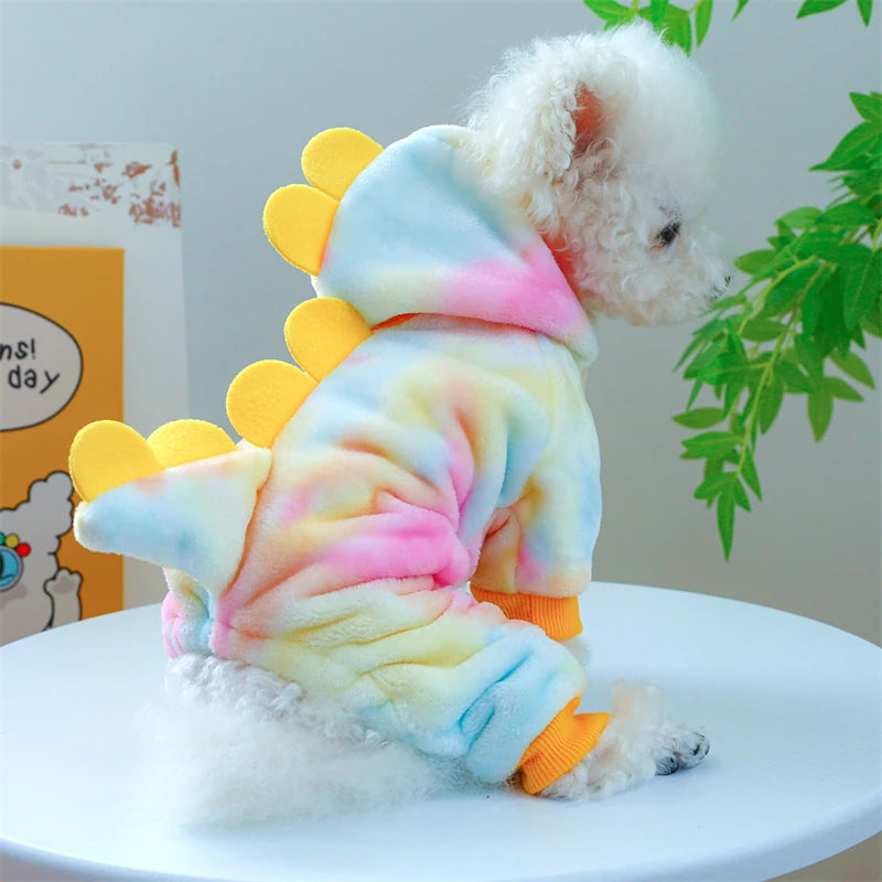 A fluffy white dog wearing a colorful, multi-colored fleece pet overcoat with yellow accents.