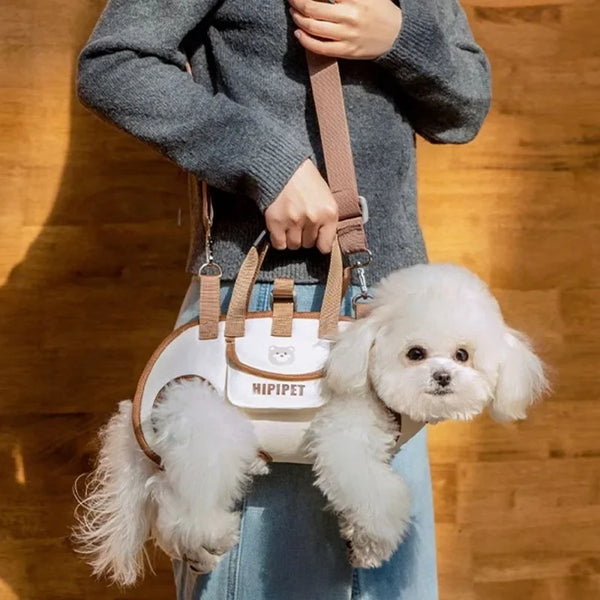 A fluffy white dog is being carried in a beige and white adjustable multi-way carrier bag by a person.