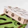 A light beige sisal cat scratching post with holes and wooden pegs resting on a green felt background.