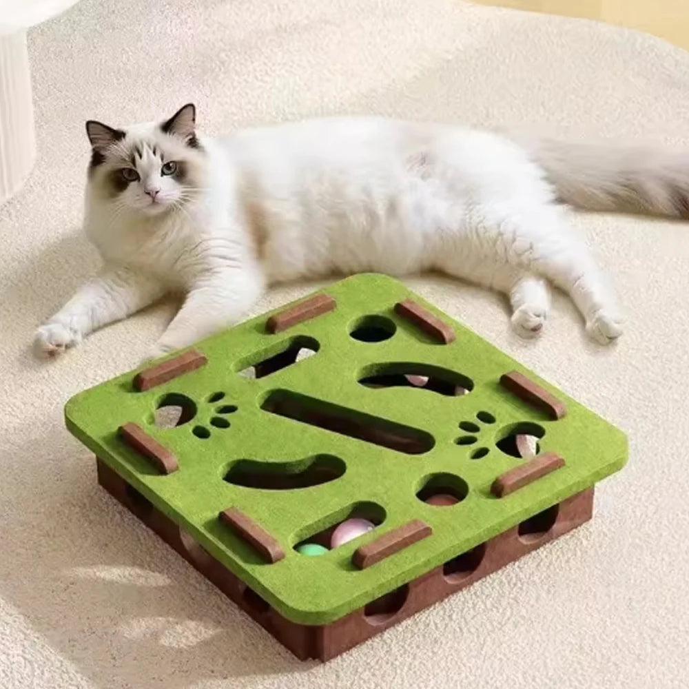A white cat is lying next to a green wooden scratching post filled with sisal and bell balls.
