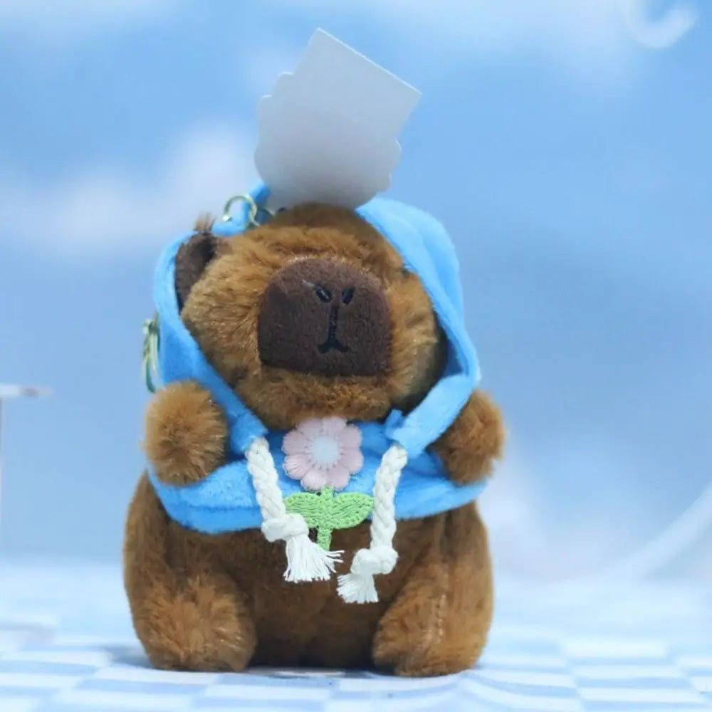 Braune Capybara-Plüschpuppe mit blauem Hoodie und weißen Flügeln.