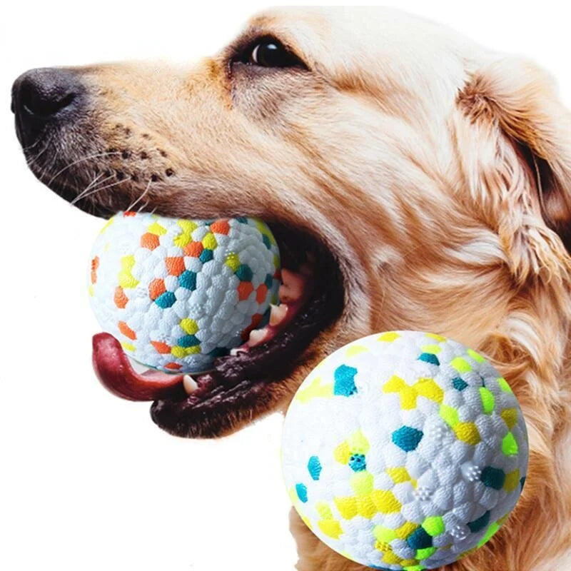 A golden retriever holds a textured, multi-colored popcorn ball toy in its mouth.