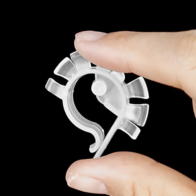 A hand holds a clear U-shaped aquarium hose clip for tubing against a black background.