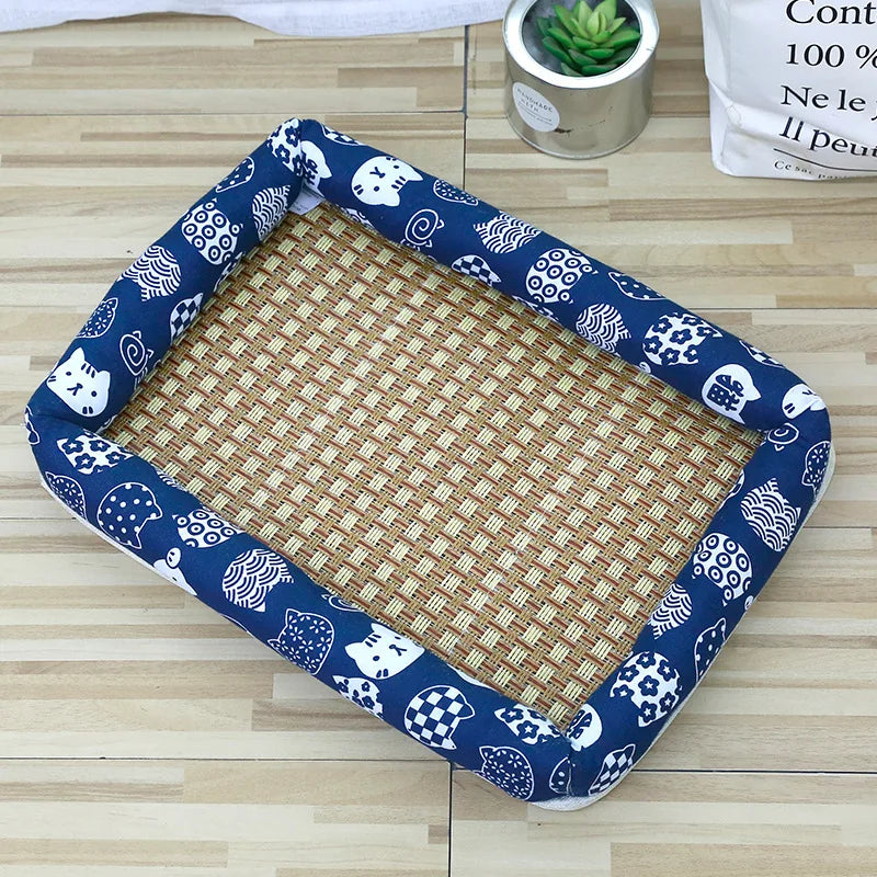 A square pet bed with a blue and white patterned border and a woven rattan mat is shown on a wooden surface.