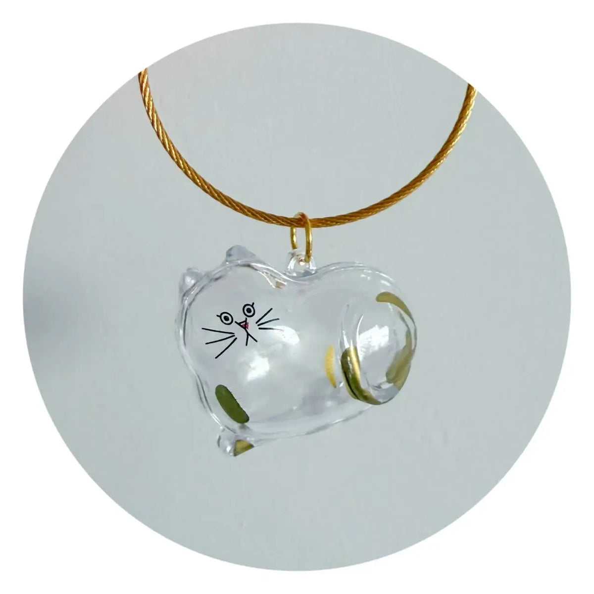 A clear glass cat charm attached to a gold-colored cord, used as a pet hair storage keychain.