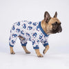 A fawn-colored dog wearing a blue and white animal print jumpsuit.