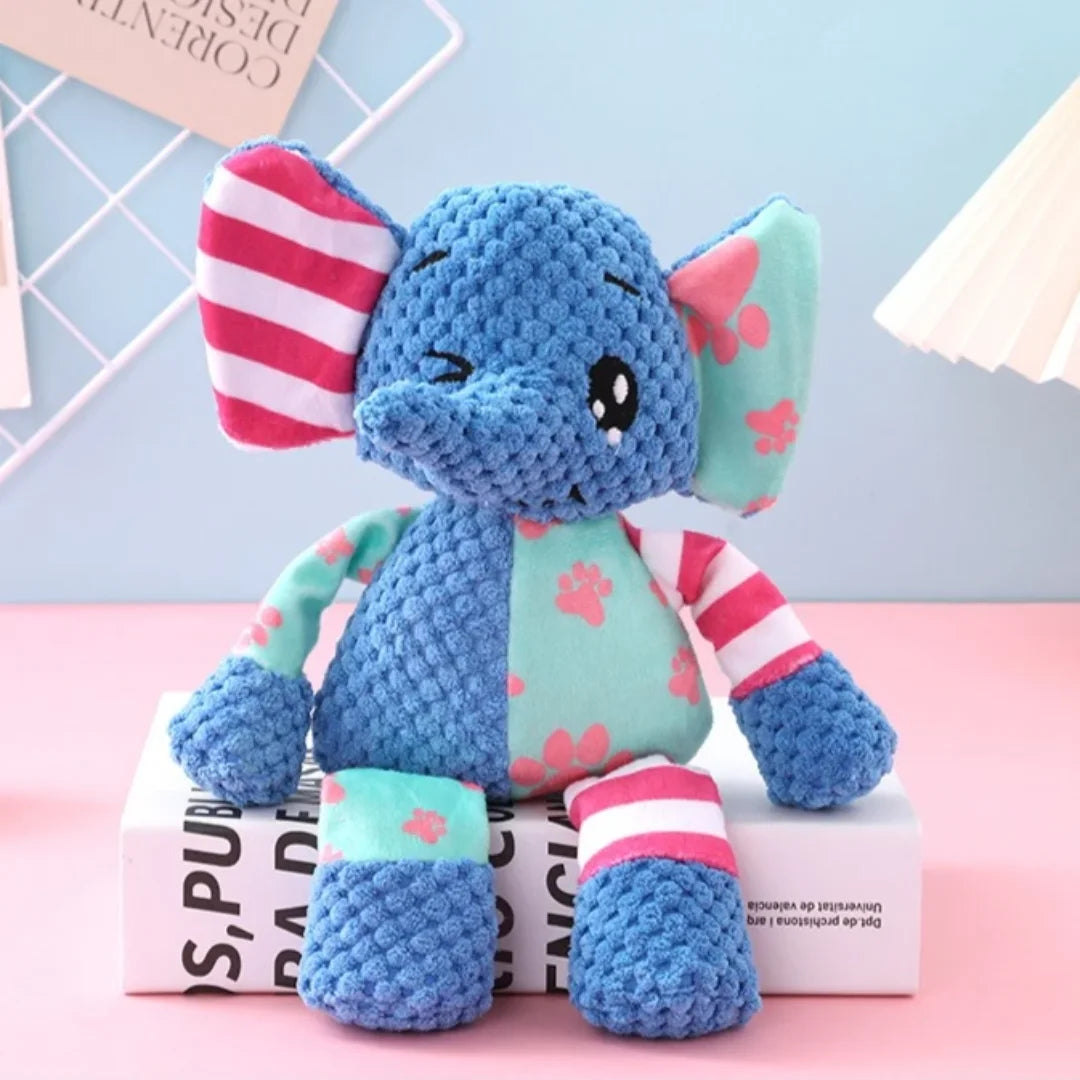 A blue elephant plush toy with pink stripes and green accents sitting on a white box.