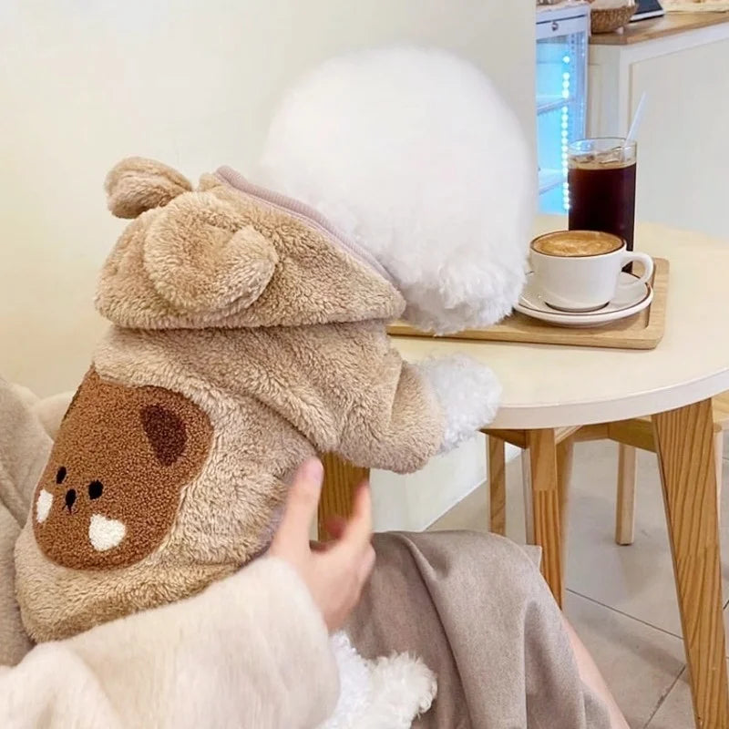 Gros plan d'un sweat à capuche pour chien en polaire beige tenu à côté d'une tasse de café.