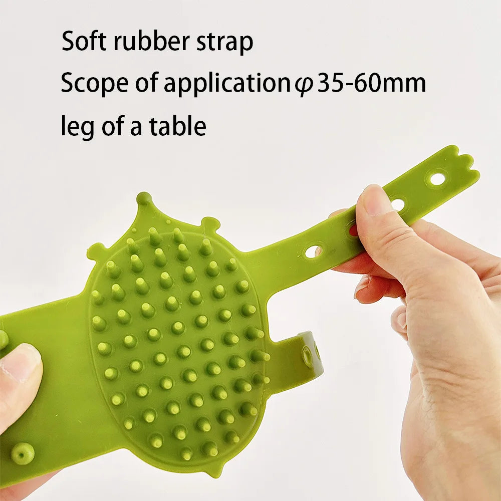 A hand holds a light green soft rubber strap pet grooming brush designed for cleaning the leg of a table.