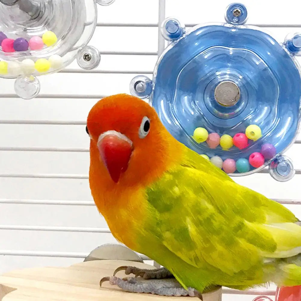 A bright orange and yellow parrot is perched in front of a blue rotating treat dispenser filled with colorful candies.