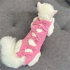 A white cat wearing a pink striped adjustable recovery vest with bow details.