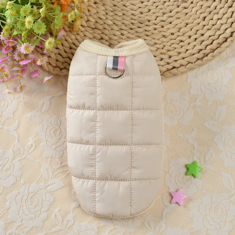 Un manteau de chien beige rembourré avec un col et une étiquette rayée, exposé sur une surface en tissu clair.