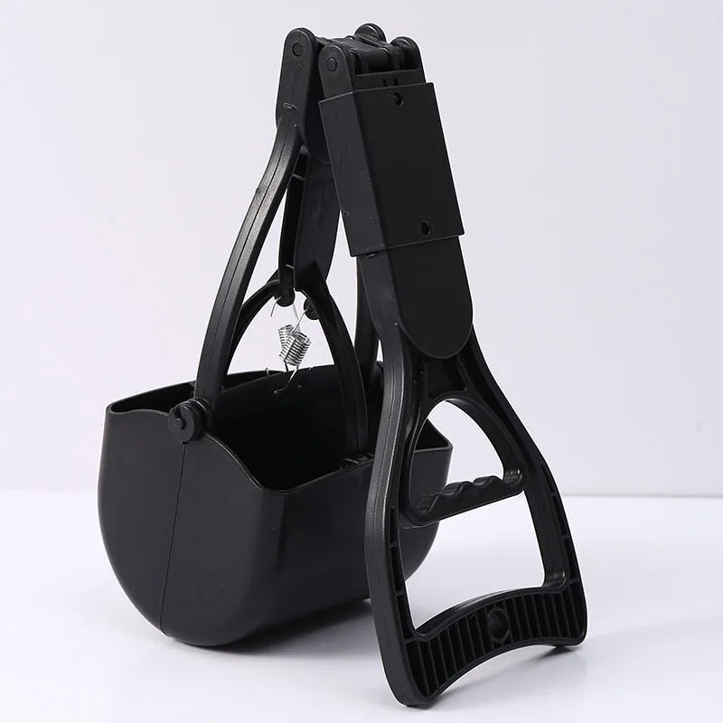 A black foldable pet poop scooper with a handle and container is shown on a white surface.