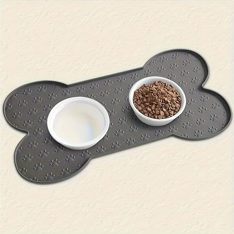 A gray silicone dog feeding mat with raised edges holds a white bowl and a bowl of dry dog food.