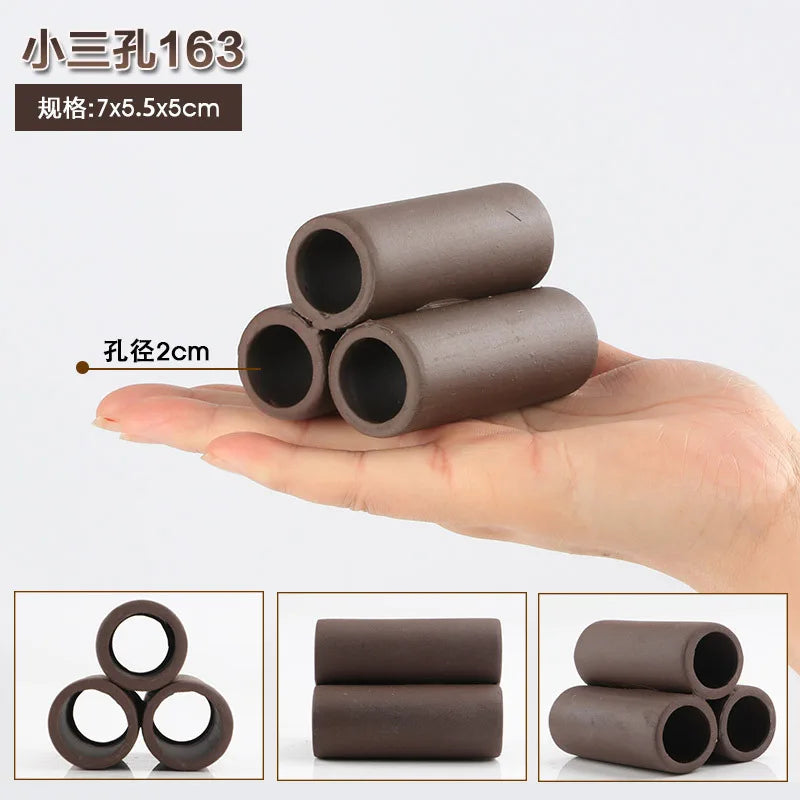 A hand holds several cylindrical natural clay aquarium cave decorations for fish and shrimp.
