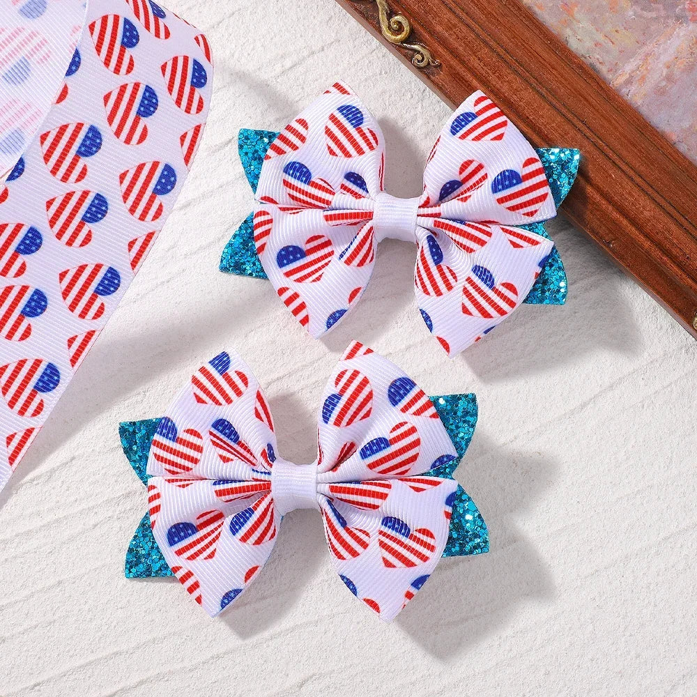 A pair of white and red patriotic star patterned ribbon hair bows with blue glitter accents displayed on a wooden surface.