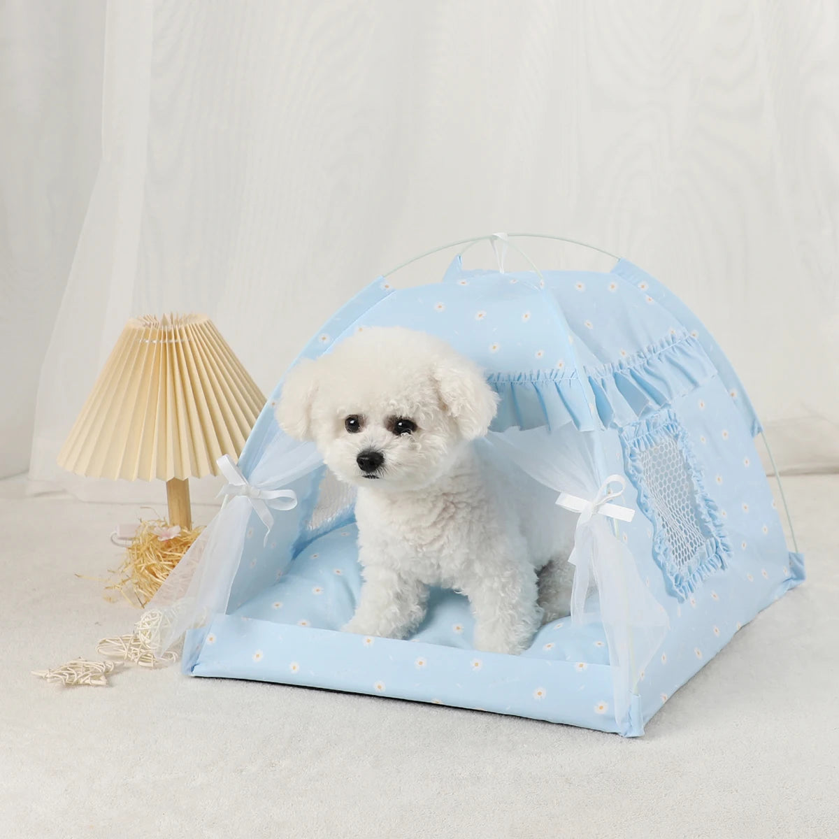 Un lit de tente pour animal de compagnie bleu clair avec tissu transparent et garniture décorative, contenant un chien blanc 