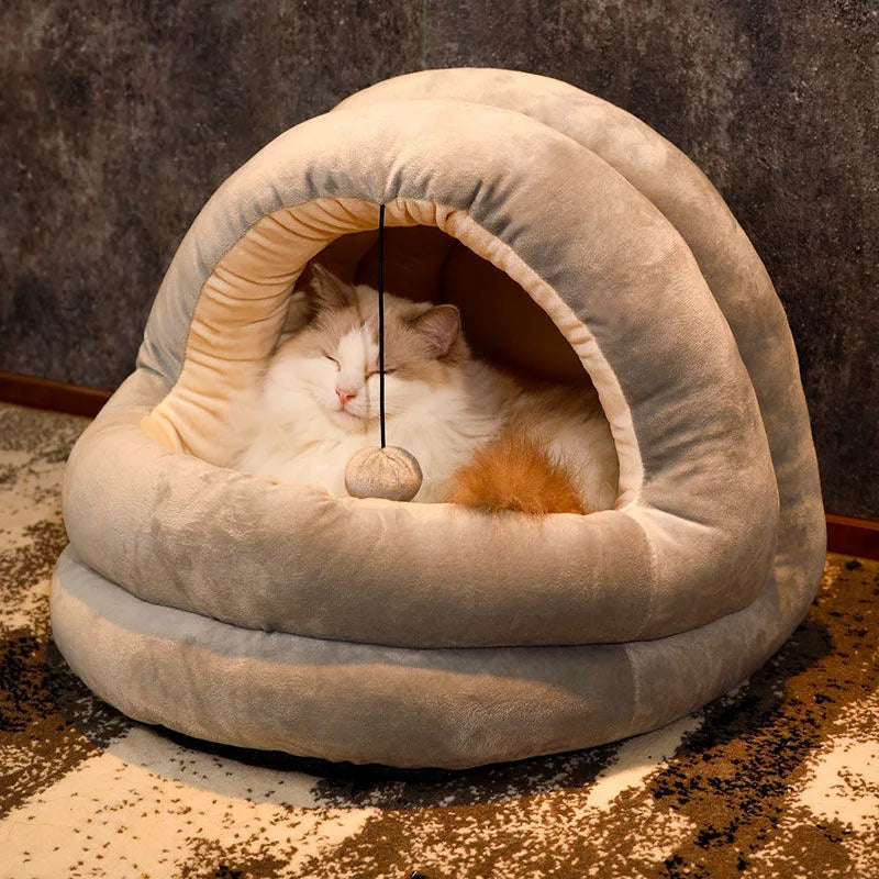 A fluffy white and orange cat is relaxing inside a beige plush cat nest bed with a hood.