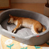 A light brown dog is resting inside a gray pet bed with a removable cushion on a yellow floral mat.