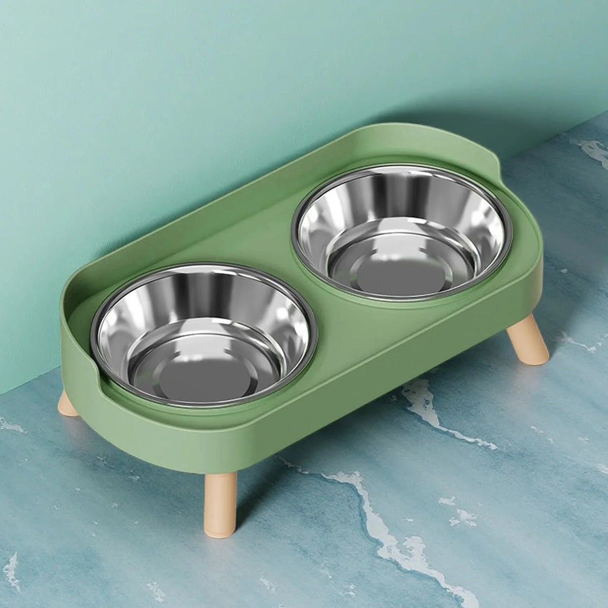 A light green elevated pet feeder with two stainless steel bowls sits on a light blue marbled surface.