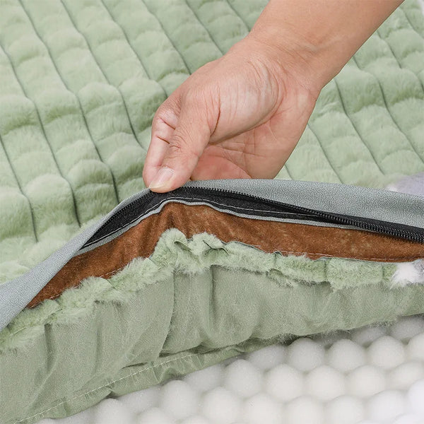 A hand is touching the seam of a green quilted dog bed with a brown faux fur lining and a black zipper.